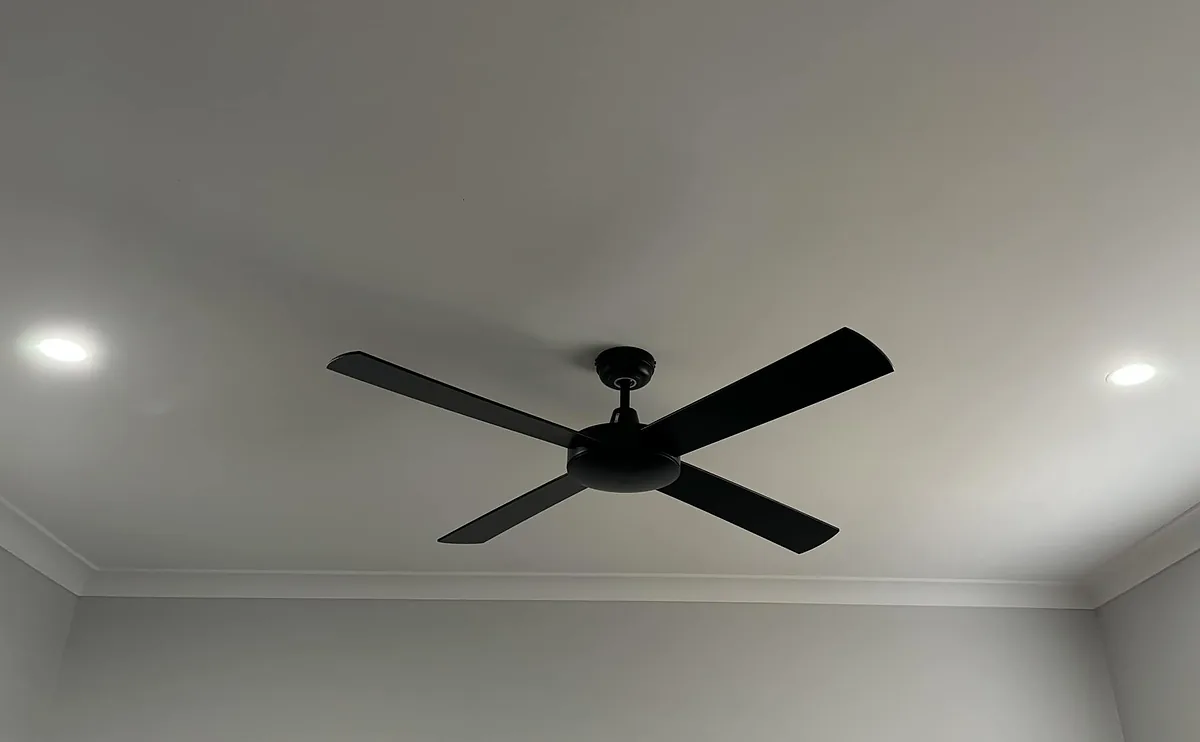 Black four blade ceiling fan between two downlights