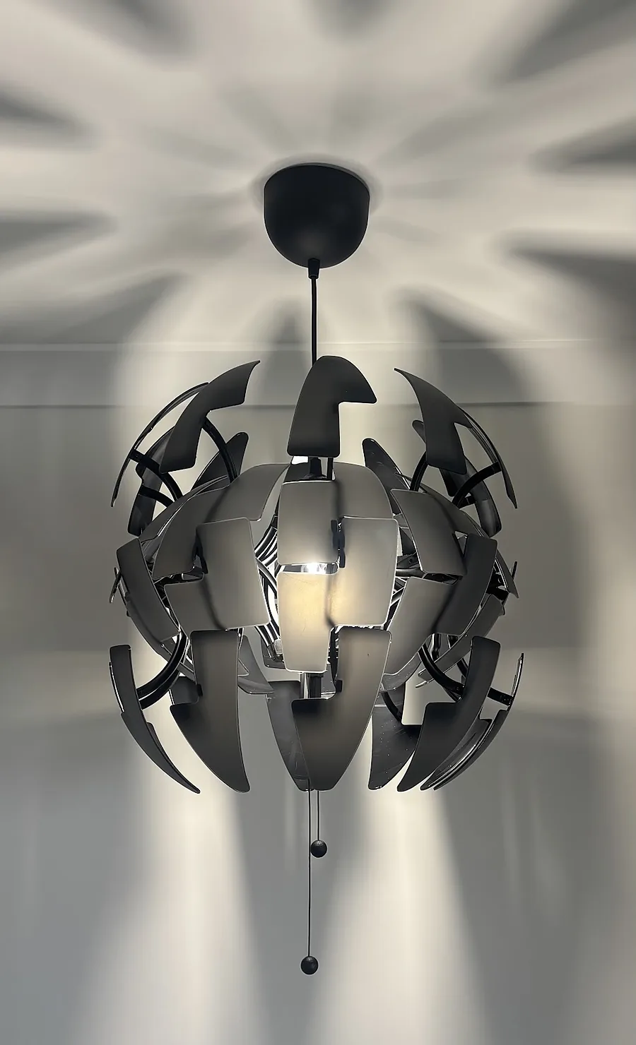 Sculptural black pendant light casting patterns on the ceiling
