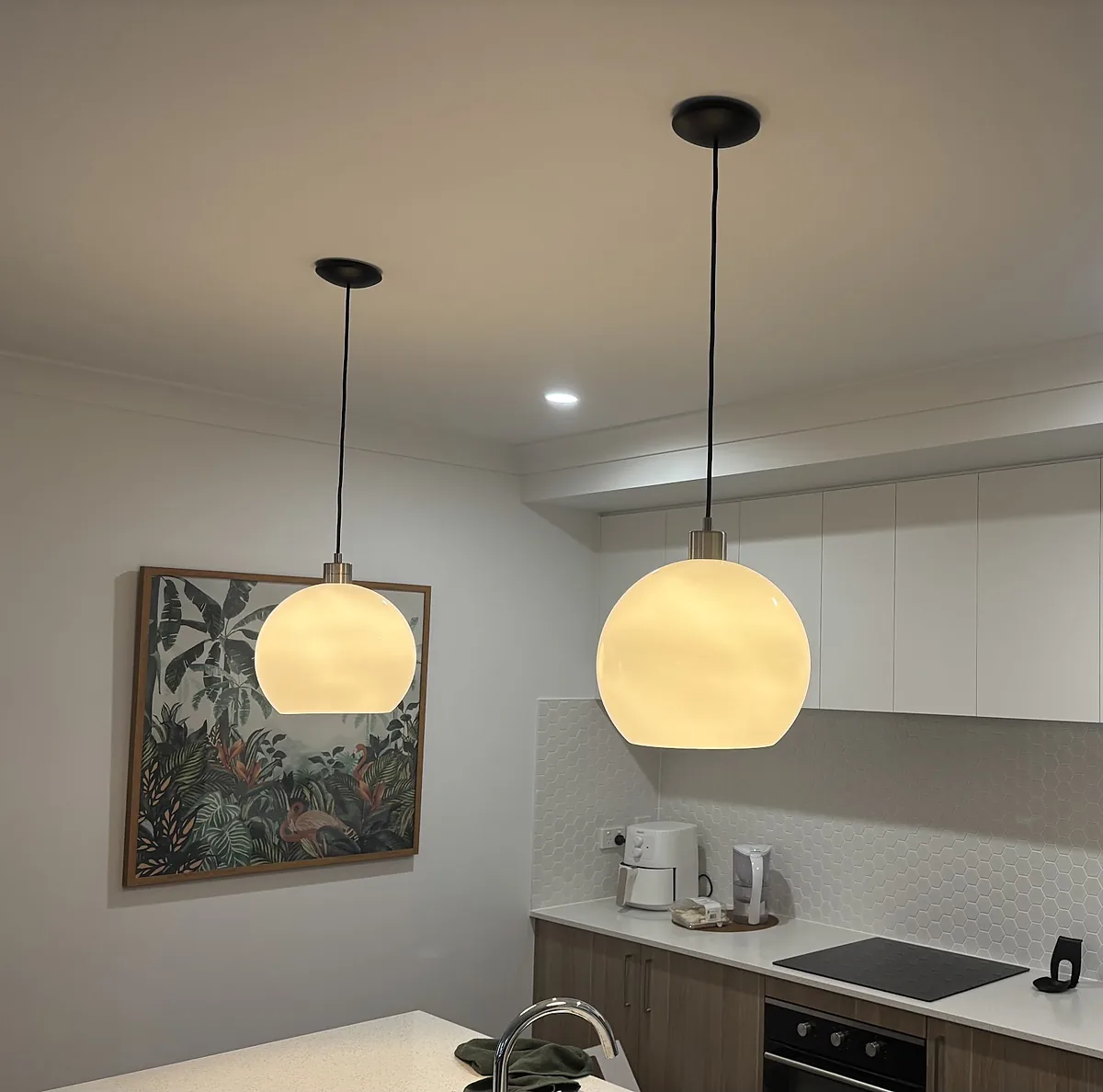 Two glass globe pendants glowing over a kitchen bench