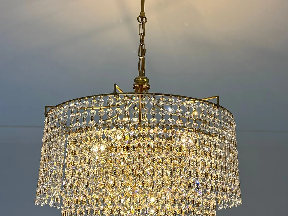 Gold and crystal chandelier glowing after installation in a grey room